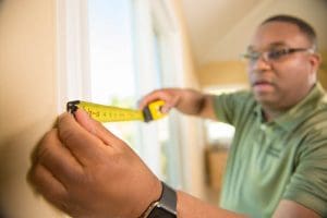 African American man measuring window with yellow measuring tape.