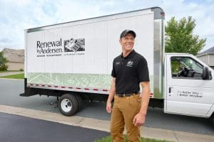 Renewal by Andersen installer wearing a black polo, black cap, and khaki pants positioned in front of a Renewal by Andersen truck