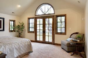 Interior of home with carpet flooring, queen size bed, and large wood frame custom windows.