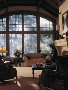 Living room with three plush couches, fireplace, and tall custom windows.