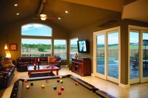 Game room with billiards table in forefront, couch and fireplace in background, and a pair of sliding modern patio doors.