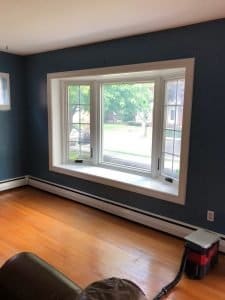 View of room with wood flooring, navy blue walls, and white-frame bay windows overlooking yard.
