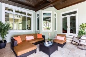Well-organized patio space with paved brick flooring, lounge-style couches, and large white frame sliding windows