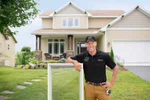 View of Renewal by Andersen employee wearing black polo and khakis leaning against a casement window while standing in front of two-story home.