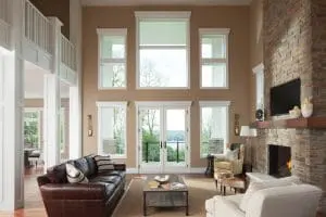 Lofty living room with brick fireplace, vaulted ceilings, and white-frame windows overlooking yard.