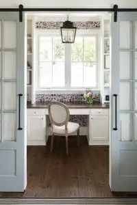 View of office with wood flooring, white desk, and white frame casement windows overlooking yard.