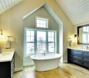 Spacious bathroom with standalone bathtub, wood flooring, and four large energy-efficient windows overlooking landscape.