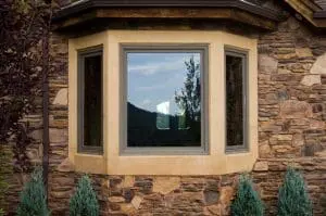Fibrex vs. Vinyl Windows Exterior of home with brick walls and large bay windows with Fibrex frames