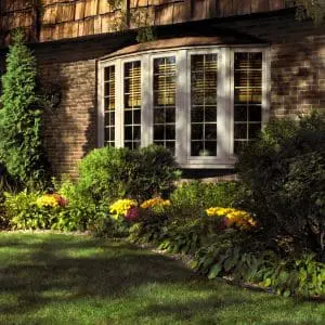 Exterior of residence featuring shrubbery, brick walls, and white bow windows.