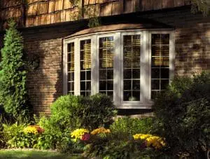 Exterior of home with brick walls, manicured shrubbery, and white bow window.