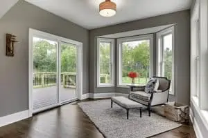 Interior of home with wood flooring, decorative rug, chair and ottoman facing a pair of sliding glass doors. Patio in background.